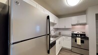 This single-floor residence offers a clean, modern aesthetic throughout its thoughtfully designed layout. The kitchen is a standout feature, showcasing white shaker-style cabinetry, granite countertops, a classic white subway tile backsplash, stainless steel appliances including a refrigerator and range, and wood-look flooring that ties the space together with a contemporary feel. A dedicated dining area adjacent to the kitchen features dark wood-look flooring and a pendant light fixture, providing a functional and stylish space for meals. The living room is bright and open, with sliding glass doors that invite natural light and provide direct access to an outdoor patio area. Two well-sized bedrooms feature plush carpeting, windows with blinds, and built-in closets offering ample storage. The two bathrooms are consistently finished with white shaker vanities, granite countertops, and wood-look flooring. One bathroom includes a tiled tub-and-shower combination with clean white tile surround. Neutral wall tones and textured ceilings are consistent throughout, contributing to a cohesive and move-in-ready atmosphere across the entire residence.