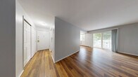 Located at 151 Andrew Ave in Naugatuck, CT, this well-appointed one-bedroom, one-bathroom residence offers a thoughtfully designed single-floor layout. Rich hardwood-style flooring runs consistently throughout the unit, lending warmth and visual continuity to every room. The combined living and dining area is generously proportioned, bathed in natural light through large sliding glass doors that open directly onto a private patio, offering pleasant outdoor views of surrounding greenery. Baseboard heating lines the perimeter of the main living spaces, ensuring year-round comfort. The galley-style kitchen is efficiently designed with white cabinetry, granite-look countertops, a speckled tile backsplash, and white appliances including a range and refrigerator, maximizing functionality within the space. The spacious primary bedroom features a wall-unit air conditioner and a large window with outdoor views. Storage is a standout feature, with three closets including a walk-in closet equipped with wire shelving. The bathroom offers a full tub-shower combination with built-in wall niches and clean white fixtures. Gray-toned walls throughout create a calm, neutral palette that complements the warm flooring for a cohesive, move-in-ready aesthetic.