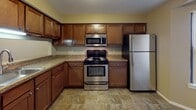 This single-floor residence offers a thoughtfully arranged layout with a range of practical features throughout. The kitchen is a functional centerpiece, finished with stone-look tile flooring, rich warm-toned wooden cabinetry, granite-style countertops, and a full suite of stainless steel appliances including a range, over-the-range microwave, refrigerator, and dishwasher. A pass-through window connects the kitchen to the living area, enhancing the open feel of the space.

The living room is a standout area, featuring vaulted ceilings, a ceiling fan with light fixture, a tile-surround fireplace, and soft carpeting underfoot. Natural light filters in through sliding glass doors, adding to the welcoming ambiance of the room.

The bedrooms are carpeted and painted in warm neutral tones, each offering dedicated closet space. The bathrooms are fitted with full tub-shower combinations accented by clean white tile surrounds and chrome fixtures.

A dedicated utility room houses a full-size top-load washer and dryer set alongside the electrical panel, providing added convenience. The mechanical room contains a furnace unit and an A.O. Smith water heater, ensuring reliable climate control and hot water supply throughout the home.