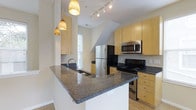 Located at 1444 Chesapeake Ave in Columbus, Ohio, this single-floor space offers a well-designed interior with a focus on modern functionality. The kitchen is a standout feature, showcasing a large granite-topped peninsula with an integrated sink, providing ample prep space and serving as a natural gathering point. Light maple cabinetry lines the walls, offering generous storage, while the dark granite countertops create a striking contrast throughout the kitchen. Stainless steel appliances, including a refrigerator, microwave, and black gas range, round out the fully equipped cooking space. Track lighting along the ceiling ensures the kitchen is well-lit, complemented by a trio of warm, woven pendant lights that hang above the peninsula, adding a decorative touch. Natural light filters in through a nearby window, brightening the space and enhancing its open feel. The light hardwood flooring flows throughout, contributing to the warm and contemporary ambiance. The overall design balances practicality with aesthetic appeal, making this a comfortable and inviting space.