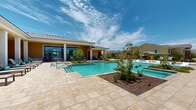 Located at 2021 Bluff Creek St in El Paso, TX, this two-floor community facility showcases a beautifully designed outdoor amenity space that serves as its centerpiece. The highlight of the property is a resort-style swimming pool with a geometric layout, complete with in-water sun loungers and integrated water features that create a relaxing, resort-like atmosphere. A connected spa sits adjacent to the main pool, offering a dedicated area for unwinding under the sunny West Texas sky. The expansive travertine-tiled pool deck provides ample space for lounging, furnished with cushioned chaise lounges, shaded umbrellas, and casual seating arrangements. Lush, drought-tolerant landscaping with native plants and ornamental trees frames the outdoor space, adding greenery and visual interest throughout. A covered colonnade along the main building offers a shaded outdoor gathering area with direct views of the pool, while large floor-to-ceiling windows and glass doors allow natural light to flow into the interior spaces. A secondary patio area features bar-height seating, ideal for social gatherings. Wrought-iron fencing encloses the entire outdoor space, providing both security and an unobstructed view of the surrounding community. The overall ambiance is bright, welcoming, and well-suited for both relaxation and community engagement.