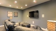 Located at 3520 Red Hook Xing in Columbus, Ohio, this single-floor residence offers a thoughtfully designed living space with a standout home theater room as a central highlight. The theater room is finished with deep slate-blue walls that set a cinematic mood, complemented by clean white baseboards that provide a crisp contrast. Recessed ceiling lighting is strategically positioned to allow for both ambient illumination and dimmed viewing conditions, enhancing the overall entertainment atmosphere. A large wall-mounted flat-screen television serves as the focal point of the room, flanked by in-wall speaker panels that suggest a built-in surround sound system for an immersive audio-visual experience. The seating arrangement features generous leather furniture, including a sectional sofa and a matching leather ottoman, providing comfortable and stylish accommodations for movie nights or gatherings. Framed theatrical artwork adorns the walls, adding character and reinforcing the room's entertainment theme. The space is designed with both function and aesthetics in mind, creating a dedicated retreat for home entertainment. The single-floor layout of the property ensures easy accessibility and a cohesive flow throughout the home.