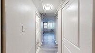 Located at 1320 W Somerville Ave in Philadelphia, PA, this one-bedroom, one-bathroom unit offers a practical and efficiently designed layout across a single floor. The space features light gray luxury vinyl plank flooring throughout, lending a clean, cohesive look to every room.

The combined kitchen and living area serves as the heart of the unit. The kitchen is outfitted with white shaker-style cabinetry, light countertops, a gas range, a refrigerator, and a sink — all arranged for functional use. A corner window placement in the kitchen brings in natural light and offers pleasant outdoor views. The living area is generously proportioned, with a wide bank of windows dressed with vertical blinds that flood the space with natural light and frame views of the surrounding neighborhood.

The bedroom is a well-sized private retreat featuring a closet with sliding doors, a window with a wall-unit air conditioner, and baseboard heating. The neutral white walls and consistent flooring create a calm, adaptable environment.

A hallway connects the main living areas to the bedroom and bathroom, providing a clear and organized flow throughout the unit. The bathroom is cleanly finished with white fixtures and tile wainscoting. Throughout the unit, white panel doors and bright overhead lighting contribute to a crisp, move-in-ready aesthetic.