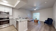 This well-appointed single-floor residence offers a thoughtfully designed open-concept layout that seamlessly connects the kitchen and living area, creating a bright and functional living environment. The kitchen is a standout feature, showcasing white shaker-style cabinetry, a classic subway tile backsplash, granite countertops, and a full suite of stainless steel appliances including a refrigerator, range, microwave, and dishwasher. A peninsula with bar seating provides additional prep space and serves as a natural divider between the kitchen and the living room. The living area is bathed in natural light through a sliding glass door that opens to a private balcony, complemented by a ceiling fan overhead. Light wood-style flooring runs throughout the entire unit, lending a clean and cohesive aesthetic. Both bedrooms are comfortably sized, each featuring large windows with roller shades for privacy and ceiling fans for year-round comfort. The bathroom is finished with granite countertops, grey shaker-style cabinetry, a large mirror, and modern fixtures. A dedicated in-unit laundry area with a washer and dryer adds everyday convenience. The overall ambiance is modern, neutral, and move-in ready.