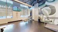 This contemporary fitness center, situated at 2350 Rue Saint-Patrick in Montreal, offers a comprehensive workout experience within its 101 square meter space. The gym is thoughtfully divided into multiple exercise zones, each catering to different fitness needs. 

The cardio area features a row of advanced treadmills, positioned in front of large windows that allow natural light to flood the space. Adjacent to this, a versatile zone houses spin bikes and other cardio equipment, overlooked by a striking wall mural depicting stylized fitness-related imagery.

The strength training section is well-equipped with a range of free weights, weight machines, and functional training apparatus. A dedicated area for bodyweight exercises and stretching is also visible, complete with mats and stability balls.

The gym's design emphasizes openness, with high ceilings and exposed ductwork contributing to an industrial-chic aesthetic. LED strip lighting runs along the ceiling, providing ample illumination throughout. The flooring appears to be a durable, dark material suitable for heavy gym use.

Large mirrors line some walls, allowing users to monitor their form during workouts. The space also includes modern amenities such as wall-mounted TVs and what appears to be a small refreshment or check-in area.

Overall, this gym combines functionality with contemporary design, creating an inviting environment for fitness enthusiasts of all levels.
