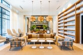 The resort clubhouse at 1031 Walnut Ave is a thoughtfully designed single-floor amenity space that blends contemporary style with warm, inviting materials throughout. The main lounge area is expansive and bathed in natural light, courtesy of floor-to-ceiling sheer-draped windows that diffuse soft, ambient illumination across the space. Mid-century-inspired seating, including high-back mustard upholstered chairs and striped accent armchairs, are arranged around a central sofa grouping beneath a cluster of woven globe pendant lights, creating an elegant yet relaxed gathering atmosphere. A full-height built-in shelving unit lines one wall, adding both visual interest and a library-like quality to the lounge.

The kitchen area features rich warm-toned wood cabinetry extending from counter to ceiling, a professional-grade range, and a striking veined stone island that serves as a functional centerpiece. Adjacent dining and café-style seating with patterned tile flooring adds a casual social dimension to the space.

The game room offers a lively contrast, equipped with a pool table, foosball table, shuffleboard, and a flat-screen TV above a built-in lounge banquette, accented by colorful artwork. Together, these zones create a well-rounded clubhouse experience suited for relaxation, socializing, and recreation.