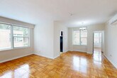 Located at 6600 Luzon Ave NW, Unit 506 in Washington, DC, this two-bedroom, one-bathroom residence offers a well-organized single-floor layout that makes efficient use of its space. Classic parquet hardwood flooring runs throughout the living areas and bedrooms, lending warmth and a timeless character to the interior.

The living room is bright and open, anchored by large windows that invite generous natural light and provide views of the surrounding greenery. Neutral walls throughout the unit create a clean, versatile backdrop. A wall-mounted air conditioning unit ensures year-round comfort.

The kitchen is equipped with rich, dark mahogany-toned cabinetry, granite-style countertops, a gas range, and a single-basin sink. A window in the kitchen allows for additional natural light and ventilation. Light ceramic tile flooring completes the space.

The primary bedroom is generously sized, featuring a corner window configuration that frames lush tree views — a notably serene feature. The second bedroom is well-proportioned with its own wall-mounted AC unit. Both rooms continue the warm parquet flooring found throughout.

The bathroom is clean and functional, featuring white subway tile walling, a tub-shower combination with chrome fixtures, and a classic black-and-white mosaic tile floor. A dedicated entrance provides a clear transition into the unit. Overall, the space presents a cohesive, practical living environment.