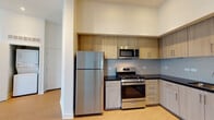 Located at 5125 Lankershim Blvd in the North Hollywood neighborhood of Los Angeles, this single-floor unit offers a contemporary design with a cohesive, modern aesthetic throughout. Light wood-style flooring runs continuously across the space, complementing the clean white walls and creating a warm, unified interior.

The kitchen is well-appointed and functional, featuring a full suite of stainless steel appliances, including a gas range, built-in microwave, refrigerator, and dishwasher. Light wood cabinetry extends to the ceiling, providing generous storage, while dark countertops and a subtle tile backsplash add contrast and visual interest. The kitchen transitions naturally into an open living area, which benefits from elevated ceilings that enhance the sense of space and airiness.

The bedroom areas are bright and serene, with large windows and sliding glass doors offering outdoor views and an abundance of natural light. At least one bedroom includes an adjoining walk-in closet with built-in shelving. The bathroom is finished in the same modern palette, with a floating wood vanity, dark countertop, and large mirror. Overall, the unit presents a clean, contemporary living environment well-suited to urban life in Los Angeles.