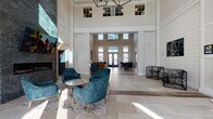 Located at 150 Country Squire in Cromwell, Connecticut, this single-story community clubhouse delivers a sophisticated and welcoming atmosphere through thoughtful architectural design and upscale interior finishes. The grand entrance features soaring double-height ceilings, shiplap-clad walls, large transom windows, and light stone tile flooring that floods the space with natural light. A striking geometric chandelier anchors the main lobby, where teal velvet armchairs, curated botanical artwork, and a stacked-stone fireplace create an inviting social hub. Adjacent seating areas offer rich caramel leather sofas beneath botanical canvas prints, providing comfortable gathering spots throughout. A dedicated conference and co-working zone features a substantial dark wood table surrounded by plush gray velvet chairs, set beneath dramatic double-height shiplap walls with ample natural light. The café and dining area showcases patterned encaustic tile flooring, white subway tile backsplash, pendant lighting, a beverage station, and wine storage — ideal for casual socializing. A game and entertainment room features warm wood-look flooring, a shuffleboard table, bold navy blue accent walls with designer wall art, and additional lounge seating. Private meeting rooms with wood-look flooring and natural light round out this well-appointed community amenity space.