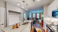 Located at 2811 Capital Blvd in Raleigh, NC, this single-floor unit showcases a contemporary design with a thoughtfully planned open-concept layout. The kitchen serves as a central hub, outfitted with crisp white cabinetry extending to the ceiling, granite countertops, a subway tile backsplash, and a full suite of stainless steel appliances including a side-by-side refrigerator, electric range, and built-in microwave. A large island with an undermount sink and geometric pendant lighting adds both function and visual interest, connecting seamlessly to the dining and living areas.

The living room is bright and welcoming, benefiting from multiple windows dressed with blinds and floor-length drapes that allow ample natural light. Warm hardwood-style flooring runs throughout the main living spaces, complemented by bold, color-blocked accent walls in olive, terracotta, and sky blue that lend an eclectic, energetic character to the interior.

The bedroom is generously proportioned, featuring plush carpet, a window with exterior views, and a striking orange accent wall. An en-suite bathroom presents granite countertops, white cabinetry, and a large vanity mirror. The overall ambiance is modern, vibrant, and well-appointed throughout.