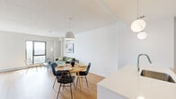 Located at 8405 Rue St-Charles in Brossard, Quebec, this single-floor unit presents a thoughtfully designed open-concept layout with a clean, contemporary aesthetic. Light hardwood flooring flows continuously throughout the main living areas, creating a warm and cohesive foundation that complements the bright white walls and ceilings.

The kitchen is a standout feature, anchored by a large central island with a white quartz countertop and an integrated sink. White cabinetry extends to the ceiling, paired with stainless steel appliances, a subway tile backsplash, and globe pendant lights that add a modern finishing touch. The kitchen opens seamlessly into the dining area, where a round wood table with woven rattan chairs sits beneath a dome pendant light, and then flows into the living room, which benefits from natural light through large windows with outdoor views.

The bedroom is a calm, well-proportioned space featuring large windows that frame outdoor views, light hardwood floors, and a full sliding closet. The bathroom maintains the unit's modern sensibility with terrazzo flooring, a wood-toned vanity with ample storage, and clean white surfaces. Overall, the unit offers a bright, functional, and stylishly minimalist living environment.