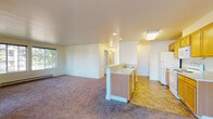 Located at 2701 Al Ogdon Way in Cheney, Washington, this single-floor unit offers a practical and well-organized layout designed for comfortable everyday living. The open-concept living and dining area is generously sized, featuring plush wall-to-wall carpeting and large windows that allow ample natural light to fill the space, with views of mature trees and the surrounding greenery. A sliding glass door connects the living area directly to an outdoor space, enhancing the sense of openness. The kitchen is efficiently designed in a galley style and opens to the living area via a peninsula with a breakfast bar. It features warm wood-toned cabinetry, a double basin sink, a full suite of white appliances including a refrigerator, electric range, built-in microwave, and dishwasher, all set on durable tile flooring. The bedrooms are carpeted and well-lit by large windows, with baseboard heating providing warmth throughout. A full bathroom includes a single vanity with wood cabinetry, a mirror, and a shower/tub combination, finished with tile flooring. Additional storage is provided through a dedicated closet with built-in wire shelving. The unit presents a clean, functional living environment in a residential Cheney neighborhood.