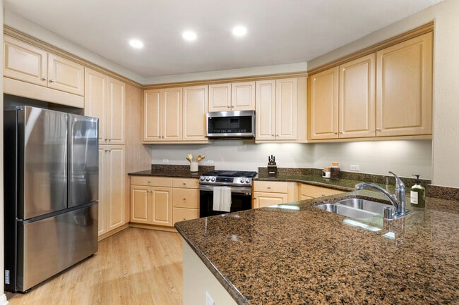 Renovated Package I kitchen with stainless steel appliances, brown speckled granite, oak cabinetry, and hard surface flooring - Avalon Encino