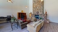 Located at 132 Fountain Oaks Circle in Sacramento, CA, this single-story community center offers an inviting and well-appointed gathering space designed for comfort and functionality. The heart of the space is a grand main hall with soaring ceilings that lend an airy, open ambiance. A floor-to-ceiling stone fireplace serves as the room's stunning focal point, crafted from natural stacked stone and rising dramatically to the full height of the wall. Light wood-style flooring runs throughout, complementing the neutral tones of the space. Ample seating areas are arranged around the fireplace, creating a warm and welcoming atmosphere ideal for community gatherings. Large, vertically stacked windows in the dining area flood the space with natural light and offer direct views of the outdoor pool and surrounding greenery, seamlessly connecting the interior to the exterior environment. A separate kitchen is well-equipped with warm oak cabinetry, granite tile countertops, a matching granite breakfast bar, a decorative coffered ceiling light fixture, and a full suite of appliances. The kitchen's pass-through layout allows for easy serving and interaction with the main hall. Overall, the space combines practical amenities with striking architectural details to create a versatile and impressive community facility.