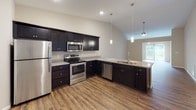 Located at 410 S Noyer Rd in Fort Wayne, Indiana, this single-floor home offers a thoughtfully designed layout with a cohesive blend of comfort and functionality. The open-concept kitchen is a standout feature, showcasing dark espresso cabinetry, granite-look countertops, stainless steel appliances, and rich hardwood-style flooring. Pendant lighting accents the peninsula, while vaulted ceilings lend an airy, spacious feel to the cooking and dining area. A dedicated pantry with wire shelving provides generous storage.

The living area continues the warm hardwood-style flooring and is bathed in natural light through a large sliding glass door that opens to outdoor views, complemented by a ceiling fan overhead. Multiple bedrooms feature plush carpeting, ceiling fans with integrated lighting, and windows that invite natural light. The primary bedroom connects to a spacious walk-in closet outfitted with multi-tiered wire shelving for ample organization.

Both bathrooms are finished with dark vanity cabinetry, granite-look countertops, and hardwood-style flooring. One bathroom includes a walk-in shower, while the other offers a full shower-tub combination. Neutral warm-toned walls throughout the home create a clean, inviting atmosphere that is both versatile and welcoming.