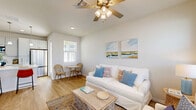 Located at 1901 N Williamson Blvd in Daytona Beach, Florida, this two-story home offers a well-designed layout across two floors, blending coastal charm with modern finishes. The main level features a bright living room with light wood flooring, a ceiling fan, and large windows that fill the space with natural light. Coastal-inspired artwork and neutral tones create a relaxed, inviting ambiance. The kitchen stands out with crisp white shaker cabinetry, a white quartz waterfall island with bar seating, stainless steel appliances, a subway tile backsplash, and pendant lighting overhead. A dedicated office on the main level offers two windows with outdoor views and ample shelving, making it an ideal workspace. A convenient half bathroom with wood-look flooring and matte black fixtures completes the lower level. Upstairs, two carpeted bedrooms provide comfortable retreats, each with ceiling fans and wall-mounted televisions. The primary bedroom includes an en suite bathroom, while the second bedroom enjoys neighborhood views through double windows. Two additional full bathrooms feature light wood-look flooring, white tile surrounds, and gray cabinetry. The home also includes a private backyard, offering outdoor space to enjoy the Florida climate.