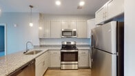Located in Shrewsbury, MA, this single-floor residence offers a thoughtfully designed layout with modern finishes throughout. The open-concept living and kitchen area is anchored by warm hardwood-style flooring that flows seamlessly between spaces. The kitchen is outfitted with white shaker-style cabinetry, granite countertops, a full suite of stainless steel appliances including a refrigerator, range, microwave, and dishwasher, and is accented by stylish pendant lighting. A kitchen island or peninsula provides additional prep space and serves as a natural divider between the kitchen and the living area. The living space is bright and open, featuring a sliding glass door with vertical blinds that leads to an outdoor area and allows natural light to fill the room. The bedrooms feature plush carpeting, neutral wall tones, and generous closet space, including a walk-in closet in the primary bedroom. The bathroom is cleanly appointed with tile flooring, a granite-topped vanity, and accessibility features including a grab bar. Throughout the residence, a consistent neutral color palette and clean architectural lines create a calm, contemporary ambiance well-suited for comfortable everyday living.