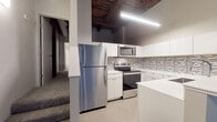 Located on Prospect Avenue East in Cleveland, OH, this loft-style unit masterfully blends historic industrial character with contemporary finishes. The defining architectural feature is the dramatic exposed wood beam and plank ceiling, which soars overhead throughout the main living area, lending warmth and a distinct warehouse-era aesthetic to the space.

The open-plan living area is generous and flexible, anchored by rich dark hardwood flooring that flows seamlessly throughout. Original timber columns punctuate the space, reinforcing the building's historic bones while complementing the modern, neutral palette of the walls.

The kitchen is well-appointed and efficiently designed, featuring crisp white cabinetry, a mosaic tile backsplash, light-toned countertops, and a full suite of stainless steel appliances including a refrigerator, range, and over-the-range microwave. A peninsula with a built-in sink provides additional prep space and a natural division between the kitchen and living areas. The kitchen is finished with light tile flooring, offering a clean contrast to the hardwood elsewhere.

A bright bedroom benefits from large windows that frame views of the surrounding urban streetscape, allowing natural light to fill the room. The bathroom is finished in a clean, all-white palette with a combination tub and shower, a vanity with under-sink storage, and tile flooring.