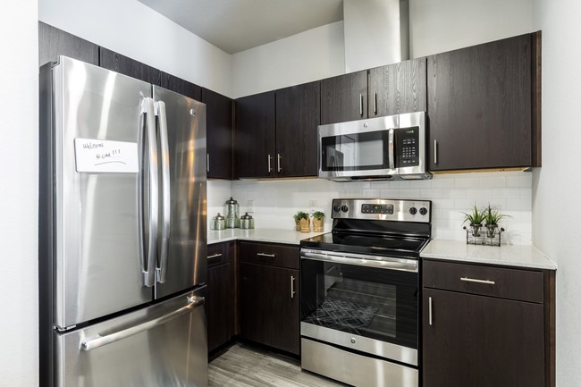 Kitchen with dark cabiets, stainless steel appliances, quartz countertops, and subway tile backsplash - Urban North