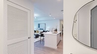 Located at 1991 Main St in the heart of Sarasota, FL, this thoughtfully designed 2-bedroom, 3-bathroom single-floor residence offers a refined contemporary living experience. The open-concept layout connects the kitchen, living, and dining areas into a seamless, light-filled space with warm wood-look flooring throughout. The kitchen is outfitted with flat-panel cabinetry in natural wood and white tones, stainless steel appliances, under-cabinet lighting, and a central island with a sink — ideal for both everyday cooking and entertaining. The living room is bright and airy, anchored by recessed and track lighting, and flows naturally into the dining area, where floor-to-ceiling black-framed windows frame stunning views of a resort-style pool and tropical palms, illuminated by a striking gold sputnik chandelier. The primary bedroom is a well-appointed retreat, and both bedrooms feature crisp white walls and ample natural light. The three bathrooms are finished with large-format marble-style tile flooring, light wood vanities, and clean white countertops, with one full bath showcasing a frameless glass walk-in shower with floor-to-ceiling tile surround. A dedicated closet and hallway complete the efficient, well-organized floor plan of this polished Sarasota residence.