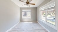 This single-floor residence has been carefully updated with a cohesive modern aesthetic that is immediately apparent upon entry. The front entry area welcomes guests with light luxury vinyl plank flooring and neutral gray walls accented by crisp white baseboards and trim — a design theme that carries consistently throughout the home. Large windows in the front-facing room flood the space with natural light and offer exterior views, while a ceiling fan adds both function and character overhead. The open living area connects seamlessly to adjoining rooms, creating a functional and airy flow. The kitchen features gray shaker-style cabinetry paired with white quartz countertops, a white subway tile backsplash, a stainless steel undermount sink with a brushed nickel pull-down faucet, and stainless steel appliances including a dishwasher and refrigerator. The bathroom is a standout space, showcasing large-format marble-look porcelain tile lining the tub surround, lending an upscale, spa-like ambiance. Bedrooms are generously proportioned with the same light flooring and soft gray walls, offering a calm and versatile backdrop. Textured ceilings, recessed lighting, and consistent HVAC venting complete the well-appointed interior of this move-in ready home.