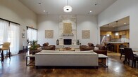 This expansive single-story space is thoughtfully designed to accommodate a variety of social and leisure activities, combining upscale finishes with a warm, inviting ambiance. The main lounge area serves as a central gathering point, anchored by a dramatic floor-to-ceiling limestone fireplace flanked by decorative wall art. Soaring ceilings amplify the sense of openness, while polished stained concrete floors flow consistently throughout, lending an industrial-yet-refined character to the space.

The fully equipped kitchen features warm wood cabinetry, granite countertops, a large center island with bar seating, stainless steel appliances including a professional-grade range hood, and a subway tile backsplash. An adjacent dining nook with pendant lighting and direct outdoor access provides a more intimate setting.

A second lounge area with vibrant terracotta accent walls and built-in media capabilities offers a casual retreat, complete with leather seating and a bar-height counter. Smaller bistro-style seating areas benefit from generous natural light through tall, sheer-draped windows with outdoor views.

A dedicated private theater features deep blue walls, plush leather reclining seats, classic movie poster décor, a granite-topped concession counter, and dramatic accent lighting, creating an immersive cinematic experience within the space.