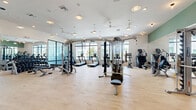 Located at 1830 Homerun Rd in Kissimmee, FL, this modern fitness center is thoughtfully designed to support a comprehensive workout experience across a generously sized single-floor layout. The space is divided into two primary areas: a main gym floor and a dedicated multi-purpose studio.

The main gym area is bright and open, featuring light hardwood-style flooring, high ceilings with ceiling fans and recessed lighting, and expansive floor-to-ceiling windows that flood the space with natural light and provide views of the surrounding community. The gym is outfitted with a full suite of Hoist strength machines, cable systems, free weights, and multiple True-brand treadmills and cardio equipment. Full-length mirrors line one wall, while decorative artwork and a vibrant tropical mural near the entry add visual character to the space.

The adjacent studio room is equally bright, with large glass doors that open directly to the outdoor patio area, creating a seamless indoor-outdoor connection. This open, airy room is equipped with battle ropes, medicine balls, kettlebells, and resistance bands stored on a dedicated rack — well-suited for functional training and group fitness classes. A wall-mounted television and built-in speakers complete the studio's amenities, making it versatile for guided workouts or independent training sessions.