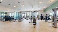 Located at 1830 Homerun Rd in Kissimmee, FL, this modern fitness center is thoughtfully designed to support a comprehensive workout experience across a generously sized single-floor layout. The space is divided into two primary areas: a main gym floor and a dedicated multi-purpose studio.

The main gym area is bright and open, featuring light hardwood-style flooring, high ceilings with ceiling fans and recessed lighting, and expansive floor-to-ceiling windows that flood the space with natural light and provide views of the surrounding community. The gym is outfitted with a full suite of Hoist strength machines, cable systems, free weights, and multiple True-brand treadmills and cardio equipment. Full-length mirrors line one wall, while decorative artwork and a vibrant tropical mural near the entry add visual character to the space.

The adjacent studio room is equally bright, with large glass doors that open directly to the outdoor patio area, creating a seamless indoor-outdoor connection. This open, airy room is equipped with battle ropes, medicine balls, kettlebells, and resistance bands stored on a dedicated rack — well-suited for functional training and group fitness classes. A wall-mounted television and built-in speakers complete the studio's amenities, making it versatile for guided workouts or independent training sessions.