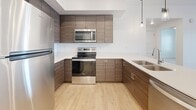This single-story residence at Daro Drive in Herriman, Utah presents a clean, modern aesthetic carried consistently throughout its layout. Light wood-look flooring runs through the main living areas, complemented by crisp white walls and recessed lighting that collectively create a bright, open atmosphere.

The kitchen is a standout feature, outfitted with flat-front cabinetry in a warm wood-grain finish, white quartz countertops, and a full suite of stainless steel appliances including a refrigerator, range, microwave, and dishwasher. A peninsula provides additional prep and seating space, while pendant lighting adds a polished detail overhead.

The living area benefits from a ceiling fan and a sliding glass door with vertical blinds that introduces natural light and provides outdoor access. Bedrooms are carpeted for comfort, with one featuring a multi-panel window and ceiling fan, and another offering direct access to a generously sized walk-in closet with built-in shelving and hanging rods.

The bathroom is finished with wood-toned cabinetry, a white quartz vanity top, a large wall mirror, and a tiled tub-shower combination set on wood-look flooring. A dedicated in-unit laundry area houses a full-sized washer and dryer with overhead shelving, adding practical convenience to the well-appointed layout.