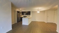This single-floor space showcases an open-concept layout that seamlessly connects the kitchen, dining, and living areas. The kitchen is outfitted with stainless steel appliances, including a refrigerator, microwave, and range, complemented by dark espresso cabinetry and a light-toned peninsula that provides additional counter space and casual seating. A tile backsplash adds a refined touch to the cooking area, while track lighting overhead ensures the workspace is well lit. The peninsula transitions naturally into the dining area, which is highlighted by a pendant light fixture that anchors the space with a warm, inviting glow. Rich, dark hardwood flooring extends throughout the entire open area, providing a cohesive and polished aesthetic. The living area offers generous room for furnishings, with neutral-toned walls creating a clean, versatile backdrop. The open sightlines between all three areas enhance the sense of spaciousness, making the layout feel both functional and welcoming. Overall, the space combines practical design with modern finishes for a comfortable, move-in ready environment.
