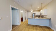 This well-appointed single-floor residence in Sellersburg, Indiana, offers a thoughtfully designed open-concept layout that seamlessly connects the kitchen and living areas. The kitchen serves as the focal point of the space, showcasing crisp white shaker-style cabinetry, granite countertops, and a full suite of stainless steel appliances including a refrigerator, electric range, and over-the-range microwave. A peninsula with pendant lighting above provides additional prep space and casual seating, making it ideal for both cooking and entertaining. Warm wood-look luxury vinyl plank flooring runs throughout the main living areas, adding a cohesive and contemporary feel. The bedroom is generously sized, featuring plush carpet, a ceiling fan with integrated lighting, and a window that allows natural light to filter in. The bathroom is cleanly finished with a rich dark wood vanity, granite countertop, undermount sink, and a full tub-shower combination. A dedicated utility room houses a full-size washer and dryer alongside the water heater and HVAC system, providing convenience and practicality within the unit. Recessed lighting and a neutral color palette throughout create a bright, inviting ambiance across the entire space.