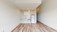 Located at 5460 N Interstate Ave in Portland, Oregon, this one-bedroom, one-bathroom unit offers a thoughtfully designed layout making efficient use of its compact footprint. Light wood-style flooring runs throughout the entire space, creating a cohesive and clean aesthetic from room to room.

The combined kitchen and living area serves as the heart of the unit. The kitchen features white flat-front cabinetry — both upper and lower — with open shelving, a single-basin sink, a built-in microwave, and a full-size refrigerator. Recessed lighting illuminates the kitchen, while the adjoining living area provides an open, flexible space with neutral walls and ample room for furnishings.

The bedroom is a bright, well-proportioned room highlighted by two large windows that frame views of the Portland cityscape and surrounding greenery. The elevated perspective and generous natural light make this room a standout feature of the unit.

The bathroom is finished in a clean, minimalist style with wood-look tile flooring, a white vanity with modern hardware, a toilet, and a walk-in shower area. A sliding frosted-glass barn door adds a contemporary architectural detail to the hallway leading to the bathroom, enhancing the unit's modern character throughout.