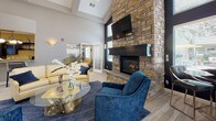 Located at 9107 W Cross Dr in Littleton, CO, this single-floor community clubhouse offers a well-appointed and thoughtfully designed gathering space. The grand entrance corridor immediately impresses with soaring vaulted ceilings accented by tray details, recessed lighting, and light wood-look tile flooring that extends throughout the space, creating a seamless and airy aesthetic.

The central lounge area serves as the focal point of the clubhouse, anchored by a striking floor-to-ceiling stone fireplace with a built-in hearth and wall-mounted television above. Vaulted ceilings with large windows allow abundant natural light to fill the room, complemented by stylish seating including plush blue accent chairs and gold-toned sofas arranged around a glass coffee table. French doors provide direct access to the outdoor area.

A dedicated meeting or office room features large windows with exterior views, carpet flooring, and a nature-inspired mountain mural, offering a functional and visually engaging workspace. The fully equipped kitchen showcases dark espresso cabinetry, granite countertops, stainless steel appliances including a French door refrigerator with ice maker, dishwasher, and a deep basin sink — ideal for hosting events or resident use. A beverage station is also conveniently located near the entry corridor, rounding out this well-equipped community amenity space.