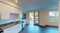 Located at 1551 Pacific Ave in Santa Cruz, California, this single-floor unit offers a contemporary design with clean lines and modern finishes. The open-concept layout is anchored by dark hardwood-style flooring that flows seamlessly throughout the space, complementing the crisp white walls and recessed lighting overhead.

The kitchen is a standout feature, outfitted with white flat-front cabinetry extending to the ceiling for ample storage, dark stone countertops, and a full suite of stainless steel appliances including a refrigerator, range, built-in microwave, and dishwasher. The layout provides generous counter space and functional workflow for everyday use.

The living area is bright and open, benefiting from natural light streaming through large windows and a sliding glass door that leads to a private balcony with outdoor views of surrounding greenery. The bedroom is well-proportioned, featuring a large window framing tree-lined views and recessed lighting.

The bathroom is clean and functional, featuring a full tub-shower combination with white tile surround and chrome fixtures. Throughout the unit, the design maintains a consistent modern aesthetic with neutral tones, making it a versatile and well-appointed space in the heart of Santa Cruz.