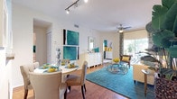 This single-story residence is defined by a cohesive and vibrant color palette of teal, yellow, and white that flows consistently throughout each room. The living room serves as the heart of the home, featuring hardwood-style flooring, a ceiling fan, and a bold yellow accent wall adorned with large-scale artwork. A sliding glass door fills the space with natural light and provides access to an outdoor patio. The kitchen is functional and well-equipped, featuring white cabinetry, dark granite-style countertops, stainless steel appliances including a dishwasher and range, and tile flooring. A convenient in-unit laundry closet with a full-size washer and dryer is located just off the kitchen. The adjacent dining area accommodates a round table with seating for four and transitions seamlessly to surrounding living spaces via open archways. The primary bedroom features plush carpeting, a teal accent wall, a ceiling-height window with natural light, and direct access to a private bathroom. A second bedroom, also carpeted, includes an open closet and its own accent wall. A full bathroom with tile flooring and a shower-tub combination serves the secondary spaces.
