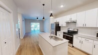 Located at 2700 Emerald Green Way in Knoxville, TN, this 1-bedroom, 1-bathroom unit offers a thoughtfully designed single-floor layout with modern finishes throughout. The open-concept kitchen and living area serves as the heart of the home, featuring light wood-style flooring, recessed lighting, and stylish pendant lights. The kitchen is well-appointed with crisp white shaker cabinetry, a white quartz waterfall island with an undermount sink, stainless steel appliances including a gas range and refrigerator, and a classic white subway tile backsplash. The living area extends naturally from the kitchen and is bathed in natural light, with a ceiling fan overhead and a sliding glass door that opens to an outdoor view. The bedroom is carpeted for comfort and includes windows with blinds that bring in natural light, complemented by two closets — one a spacious walk-in with wire shelving. The bathroom features accessibility-conscious design with grab bars, a white vanity with a framed mirror, and warm lighting. Additional spaces include a dedicated laundry area and a utility room, rounding out the practical and functional layout of this well-finished unit.