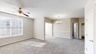 Located at 1100 Lakeridge Rd in Hampton, Virginia, this single-floor residence offers a well-designed, open layout finished in neutral warm tones throughout. The living and dining areas flow seamlessly together, both carpeted in plush neutral-toned flooring and illuminated by natural light streaming through multiple windows with blinds. The living room features a ceiling fan, while the adjacent dining space is accented by an elegant chandelier and chair-rail wainscoting, adding a refined architectural detail to the space. The kitchen is equipped with stainless steel appliances, including a refrigerator, electric range, built-in microwave, and dishwasher, all complemented by granite-look countertops and crisp white cabinetry with wood-look flooring underfoot. A dedicated laundry area with a washer and water heater is conveniently accessible directly from the kitchen. The bedrooms are carpeted and well-proportioned, each featuring mirrored sliding-door closets with built-in shelving. At least one bedroom benefits from an en-suite bathroom with white cabinetry and dark countertops. Multiple windows throughout the residence ensure consistent natural light and outdoor views, creating a bright and comfortable living environment overall.