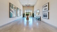 This welcoming hallway lobby at 11821 Skylark Cir in Whittier, California, makes a strong first impression with its thoughtfully designed interior and generous proportions. The space is defined by soaring ceilings that amplify the sense of openness, while polished concrete floors reflect the ambient light and contribute to a sleek, modern aesthetic throughout.

Natural light pours in through tall glass double doors at the entry, framed by floor-to-ceiling windows that offer views of the surrounding outdoor greenery. A striking sputnik-style chandelier serves as a focal point overhead, adding a touch of mid-century modern elegance to the space.

The walls are adorned with a curated selection of large-scale framed artwork, including bold abstract pieces with flowing, organic patterns as well as black-and-white photography, giving the lobby a gallery-like quality. A round pedestal table positioned centrally in the room is topped with a lush floral arrangement, creating an inviting focal point.

Additional furnishings include a classic dark wood bench and a circular gold-framed mirror, adding warmth and depth to the otherwise neutral palette of soft whites and warm beiges. Potted plants are thoughtfully placed throughout, enhancing the fresh, vibrant atmosphere. Recessed lighting complements the natural light, ensuring the space remains bright and welcoming at all times.