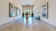 This welcoming hallway lobby at 11821 Skylark Cir in Whittier, California, makes a strong first impression with its thoughtfully designed interior and generous proportions. The space is defined by soaring ceilings that amplify the sense of openness, while polished concrete floors reflect the ambient light and contribute to a sleek, modern aesthetic throughout.

Natural light pours in through tall glass double doors at the entry, framed by floor-to-ceiling windows that offer views of the surrounding outdoor greenery. A striking sputnik-style chandelier serves as a focal point overhead, adding a touch of mid-century modern elegance to the space.

The walls are adorned with a curated selection of large-scale framed artwork, including bold abstract pieces with flowing, organic patterns as well as black-and-white photography, giving the lobby a gallery-like quality. A round pedestal table positioned centrally in the room is topped with a lush floral arrangement, creating an inviting focal point.

Additional furnishings include a classic dark wood bench and a circular gold-framed mirror, adding warmth and depth to the otherwise neutral palette of soft whites and warm beiges. Potted plants are thoughtfully placed throughout, enhancing the fresh, vibrant atmosphere. Recessed lighting complements the natural light, ensuring the space remains bright and welcoming at all times.