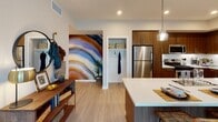 Located at 2225 Collett Ave in Corona, California, this modern single-story residence offers a thoughtfully designed open-concept floor plan that seamlessly connects the kitchen, dining, and living areas. The kitchen is a standout feature, showcasing rich walnut-toned cabinetry, white quartz countertops, a large center island with pendant lighting, and a full suite of stainless steel appliances including a gas range, dishwasher, and refrigerator. Light wood-style flooring flows throughout the main living areas, enhancing the bright and airy atmosphere. The entryway makes a bold first impression with a vibrant artistic mural accent wall and a convenient coat closet. The living room is well-appointed with large windows and a sliding glass door that invite abundant natural light and provide outdoor access. Two bedrooms offer comfortable retreats, each with plush carpeting and windows fitted with blinds and drape panels. Both bathrooms are finished with walnut vanities, white quartz countertops, large mirrors, and combination tub-shower setups with clean white tile surrounds. In-unit laundry hookups are also present. The overall design aesthetic is contemporary and cohesive, blending warm wood tones with crisp white finishes throughout.