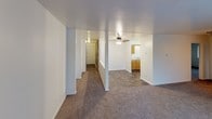 This single-floor unit offers a straightforward, functional layout with clearly defined living spaces. The living room is generously sized, featuring wall-to-wall carpet, baseboard heating units along the perimeter, and a sliding glass door that fills the room with natural light and provides access to an outdoor area. A wall-mounted air conditioning unit serves the space for year-round comfort. A ceiling fan is positioned centrally in the adjoining area, enhancing airflow throughout.

The kitchen is equipped with warm-toned oak cabinetry, a double-basin stainless steel sink, light laminate countertops, and upper cabinets with under-cabinet lighting. The kitchen opens toward the main living area, maintaining a connected feel. Hard-surface flooring in the kitchen and entry contrasts with the carpet found throughout the rest of the unit.

The bedroom is a well-proportioned, carpeted room with a standard window that allows natural light to filter in. The bathroom features a full-size soaking tub with a white surround, a shower rod, and a toilet, all set within a compact, clean space. A hallway connects the rooms, providing a logical and efficient flow throughout the unit.
