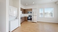 Located at 9917 NE 13th Ave in Vancouver, WA, this 2-bedroom, 1-bathroom unit offers a clean, modern design across a single floor. The open-concept kitchen and living area serves as the heart of the home, featuring rich dark wood cabinetry, white countertops, and a full suite of stainless steel appliances including a refrigerator, range, microwave, and dishwasher. A stacked in-unit washer and dryer is conveniently positioned just off the kitchen. Warm wood-look luxury vinyl flooring flows throughout the entire unit, complementing the crisp white walls and creating a bright, cohesive aesthetic. Both bedrooms are well-proportioned, with large windows that invite abundant natural light and offer exterior views. The primary bedroom includes a closet with sliding doors for organized storage, and a second closet is also available within the unit. The full bathroom is finished with a wood-toned vanity with a white countertop, a mirrored medicine cabinet, and a full bathtub with a shower and brushed nickel fixtures. The overall layout is functional and thoughtfully arranged, making efficient use of space while maintaining a fresh and contemporary feel throughout.