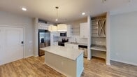 Located at 1012 Jasmine Dr in Fort Mill, SC, this single-floor residence offers a thoughtfully designed layout with modern finishes throughout. The kitchen serves as the heart of the home, showcasing white cabinetry, granite countertops, and a full suite of stainless steel appliances, including a side-by-side refrigerator with ice maker, electric range, built-in microwave, and dishwasher. A central island with pendant lighting provides additional prep space and casual seating, while open shelving and a dedicated built-in wine rack add functional character. Wood-look flooring flows throughout the main living and kitchen areas, creating a cohesive and easy-to-maintain surface. The bedroom features plush carpeting, a ceiling fan, and a window with blinds that allows natural light and outdoor views. A walk-in closet outfitted with wire shelving and hanging rods offers generous storage. The bathroom includes a granite-topped vanity with an undermount sink, a tub/shower combination, and wood-look flooring that ties into the rest of the home. The neutral color palette and clean architectural lines throughout contribute to a bright, welcoming ambiance suited for comfortable everyday living.