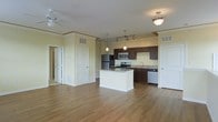 This single-floor residence offers an open and airy layout that seamlessly connects the living area to the kitchen, creating a spacious and functional environment. The kitchen is a standout feature, showcasing rich dark-toned cabinetry that contrasts beautifully with granite countertops and a suite of stainless steel appliances, including a refrigerator, microwave, range, and dishwasher. A central kitchen island provides additional prep space and serves as a natural gathering point. Pendant lighting and a track light fixture illuminate the kitchen, while a flush-mount ceiling light and ceiling fan add comfort to the living area. Warm hardwood-style flooring runs throughout the main living space, adding both elegance and practicality. Crown molding along the upper walls lends a refined architectural detail to the interior. The soft yellow-toned walls create a bright and welcoming ambiance. Multiple doorways lead to additional rooms, suggesting a thoughtful and well-organized floor plan. The overall design balances modern amenities with classic details, making this a comfortable and stylish living space.