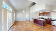 Located at 130 Hempstead Ave. in West Hempstead, NY, this well-appointed three-bedroom, two-bathroom residence spans two floors, offering a generous and thoughtfully designed living space. The main floor makes a striking impression with soaring vaulted ceilings in the open-concept living room and kitchen area, enhanced by a ceiling fan and abundant natural light from large windows. The kitchen is a standout feature, boasting rich wood cabinetry, dark granite countertops, a subway tile backsplash, stainless steel appliances, and elegant pendant lighting over a spacious island that flows seamlessly into the living area. Hardwood flooring runs throughout the main living spaces, adding warmth and continuity. The hallways are clean and bright, connecting rooms with ease. Bedrooms are carpeted and well-sized, with large windows offering views of the surrounding community. The expansive primary bedroom includes a walk-in closet with wire shelving. The bathrooms are finished with wood vanities and light hardwood-style flooring. A private balcony on the upper level offers open views of the beautifully maintained courtyard and surrounding multi-story building complex under a wide blue sky.