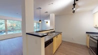 Located in Seattle's vibrant Belltown neighborhood, Unit 205 at 2201 4th Avenue is a single-floor residence designed with a clean, modern aesthetic throughout. The open-concept living area is anchored by wide plank hardwood-style flooring and a wall of large, wood-framed windows that flood the space with natural light and offer views of the surrounding urban greenery. Track lighting is installed throughout, providing versatile illumination across the main living spaces.

The galley-style kitchen is efficiently laid out with light maple cabinetry, dark countertops, a double stainless steel sink with dishwasher, and a full suite of stainless steel appliances including a refrigerator, range, and microwave. A peninsula with a breakfast bar visually connects the kitchen to the living area, with stylish pendant lighting overhead reinforcing the space's contemporary character.

The bedroom features plush carpeting, a baseboard heating unit, and multiple windows that bring in additional natural light. The bathroom is finished with tile flooring, a dual-sink vanity with dark countertops and maple cabinetry, a full mirror, and well-positioned overhead lighting. The overall design maintains a consistent, cohesive palette of neutral tones, light wood finishes, and dark accents throughout.