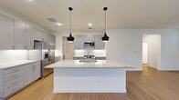 This well-designed two-story home offers four bedrooms and four bathrooms across a thoughtfully laid-out floor plan. The main level features an open-concept kitchen and living area with light hardwood-style flooring, creating a bright and welcoming atmosphere. The kitchen is a standout, showcasing a large granite-topped island with an undermount sink, sleek gray shaker cabinetry reaching to the ceiling, a subway tile backsplash, and stainless steel appliances including a gas range, microwave, and French door refrigerator. Stylish pendant lighting accents the island, completing the contemporary aesthetic. A dedicated laundry room on the upper level includes overhead gray cabinetry, a granite folding surface, and a window for natural light. The primary bedroom is generously proportioned with hardwood-style flooring, multiple windows with natural light, and a ceiling fan. Its en-suite bathroom impresses with a dual-sink granite vanity, wood-toned cabinetry, a glass-enclosed walk-in shower with tile surround, and direct access to a spacious walk-in closet with built-in shelving and hanging rods. Secondary bedrooms feature plush carpeting, while upper-level hallways are bright and open with natural light streaming through windows. Five closets provide ample storage throughout the home.