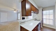 This single-story residence offers a thoughtfully arranged floor plan that balances comfort and functionality. The open-concept kitchen is a standout feature, equipped with rich dark walnut-toned cabinetry that extends to the ceiling for generous storage, a white countertop peninsula that doubles as a breakfast bar, a stainless steel refrigerator, a range, and a double sink. The kitchen flows seamlessly into the living area, which is bright and welcoming, featuring large windows that invite natural light, soft carpeted flooring, a ceiling fan with light fixture, and a classic fireplace with a clean white surround that serves as a natural focal point.

The bedrooms are well-sized, each outfitted with plush carpeting, ceiling fans, and windows that provide additional natural light. Ample closet space is provided, contributing to the overall practicality of each room. The bathrooms are finished with neutral large-format tile surrounding soaking tub-shower combinations, complemented by wood-look flooring and dark wood vanity cabinetry. Textured ceilings are consistent throughout the space, adding a subtle design element. Overall, the residence presents a cohesive, comfortable environment suited for everyday living.
