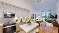 Located at 1650 NE 124th St in North Miami, this well-appointed 1-bedroom, 1-bathroom unit showcases contemporary design with a thoughtful, efficient layout. Soaring ceilings throughout amplify the sense of space, filling the interior with an airy, open ambiance. The kitchen and living area flow seamlessly together in an open-concept arrangement. The kitchen features two-tone cabinetry — combining sleek white upper cabinets with warm wood-toned lower cabinets — complemented by a subway tile backsplash, white quartz countertops, stainless steel appliances including a refrigerator, range, microwave, and dishwasher, and a central island with seating. Wide-plank hardwood flooring runs throughout the main living areas, adding warmth and continuity. The living room is anchored by floor-to-ceiling windows and a glass door opening to a private balcony, allowing abundant natural light and garden views. The generously sized bedroom offers a large window framing greenery outside, creating a serene retreat. The bathroom is finished with striking marble-look tile covering both the floors and walk-in shower walls, paired with a warm wood vanity and modern fixtures. A dedicated closet and hallway complete the functional layout of this stylish North Miami residence.