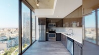Located in the heart of downtown Los Angeles, this contemporary high-rise unit at 801 S Hope St offers a sophisticated urban living experience defined by industrial-chic design and modern finishes. Exposed concrete ceilings throughout lend the space a distinctive loft-inspired character, while wide-plank hardwood flooring flows seamlessly from room to room.

The open living area is anchored by dramatic floor-to-ceiling windows and a glass-panel balcony door, flooding the space with natural light and framing sweeping views of the Los Angeles skyline. A ceiling fan completes this airy, light-filled retreat.

The kitchen is outfitted with high-gloss cabinetry in rich dark tones, stainless steel appliances including a refrigerator, range, microwave, and dishwasher, complemented by white quartz countertops and a textured tile backsplash. The expansive windows in the kitchen provide continuous panoramic city views, making it as visually striking as it is functional.

The bathroom features a deep soaking tub surrounded by clean, neutral tile work, offering a calm and refined aesthetic. Storage is well-considered throughout, with multiple walk-in closets equipped with wire shelving systems, providing generous organizational capacity. The unit's layout is efficiently designed, with a welcoming entry hallway leading to the distinct living, kitchen, and private spaces.